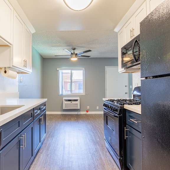 a kitchen with a black refrigerator and wooden floors.