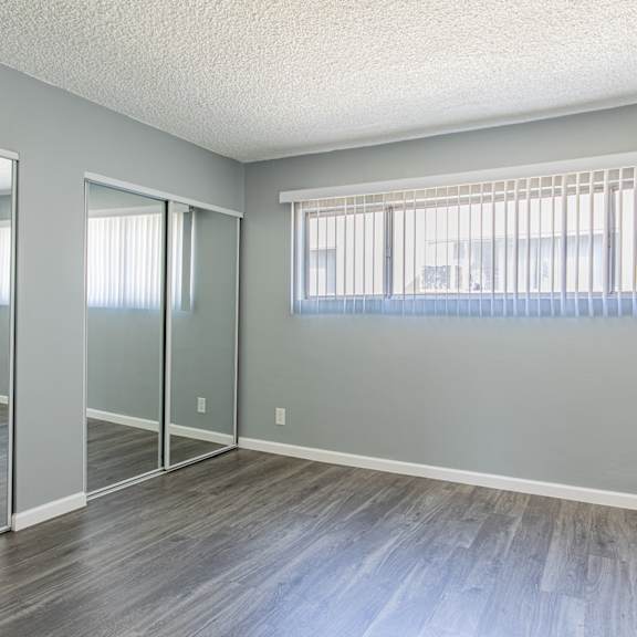 a room with grey walls and wooden flooring with a window covered by a white blind.