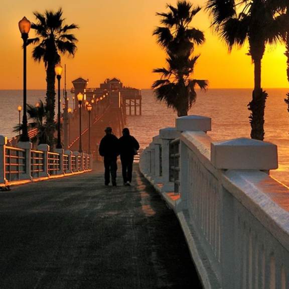 two people walking down a pier at sunset