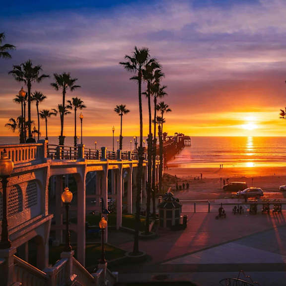 the sun sets over the beach and palm trees at the imperial beach pier