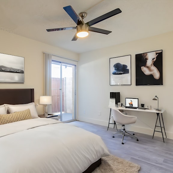 a bedroom with a large bed, a desk with a chair, and a ceiling fan.