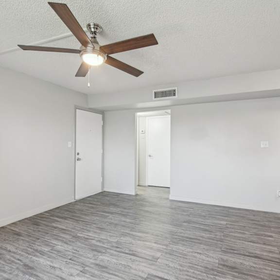 an empty living room with a ceiling fan and white walls