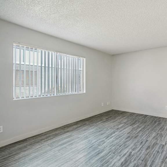 the spacious living room of an apartment with wood flooring and a window