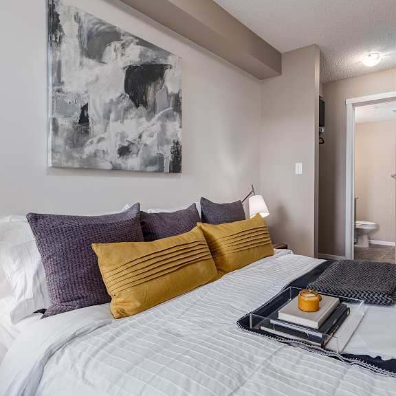 a bed with a white comforter and a tray with a candle and a book on it.