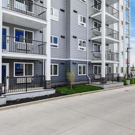 a street view of a residential area with apartment buildings on the left and a car parked on the right.