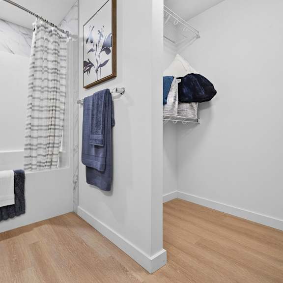 a bathroom with a white toilet, a white sink, a white bathtub, a white shower curtain, a white towel, a blue towel, a blue bag, a white shelf, a white wall,