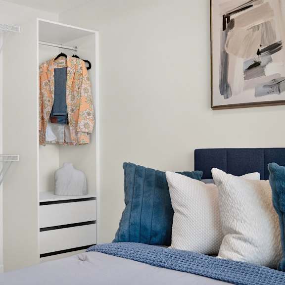a bedroom with a bed, pillows, a wardrobe, and a painting on the wall.
