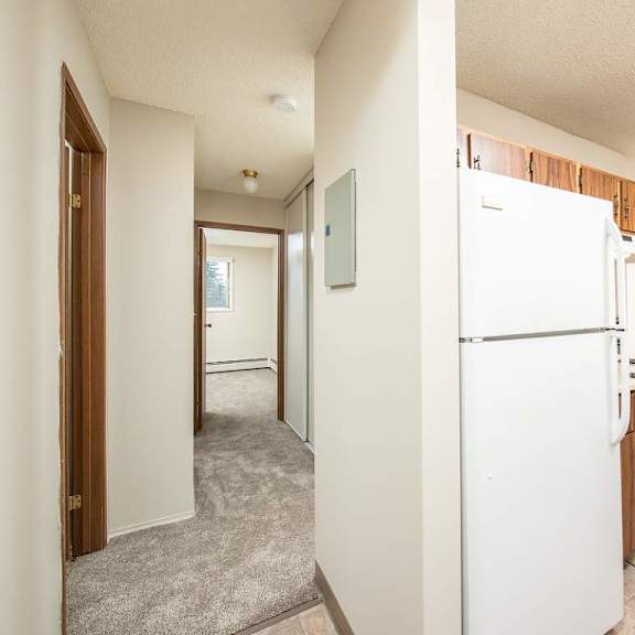 a white refrigerator in a kitchen with a white wall and a brown oven.