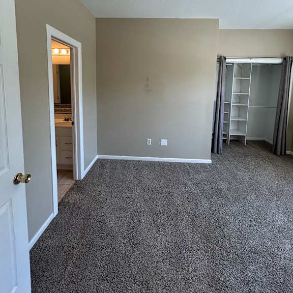a white door with a keyhole is in the foreground of a room with a window and a vent above it.