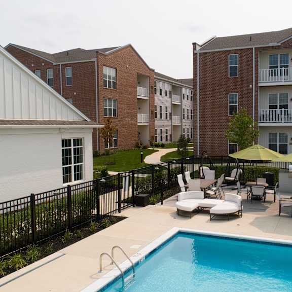 a pool surrounded by chairs and umbrellas in front of apartment buildings.