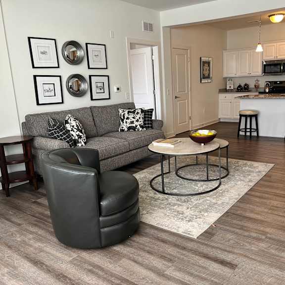a grey couch with a black leather chair and a small table in a room with wooden flooring.