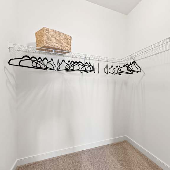 a white closet with a basket and clothes hanging on a wire rack.