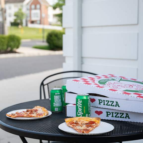a pizza box and two cans of sprite are on a table outside.