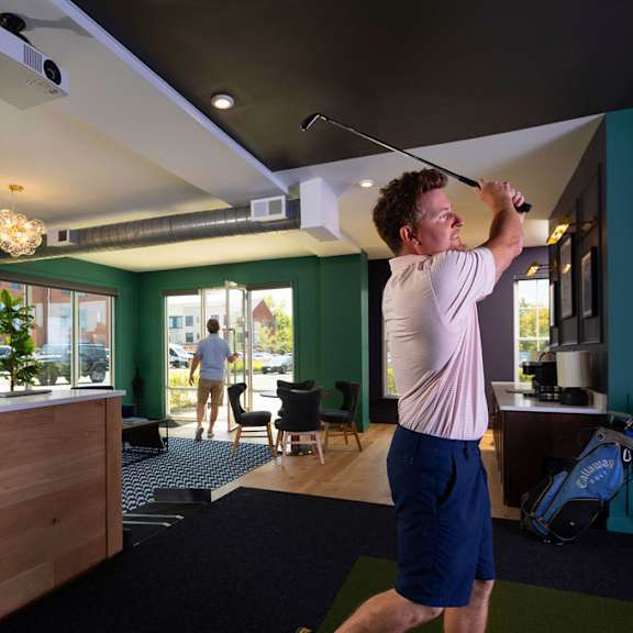a man is playing golf in a room with a green wall.