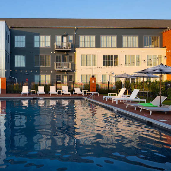 a large swimming pool in front of a building with lounge chairs around it.