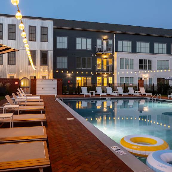 a pool with chairs and a building in the background.
