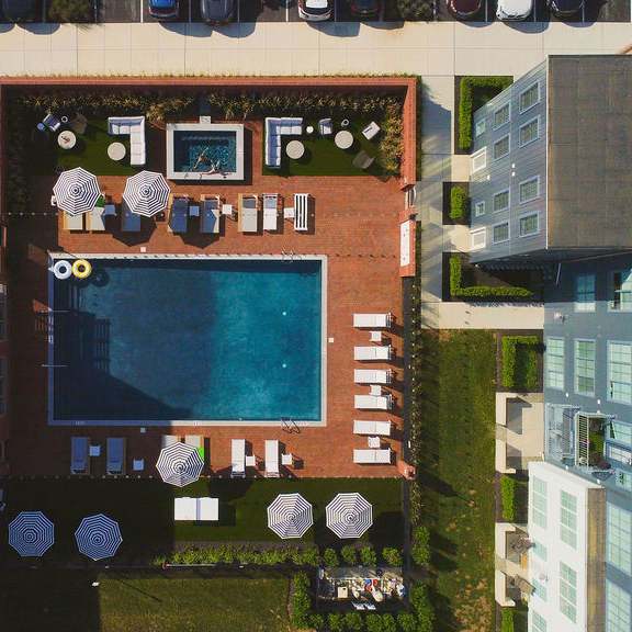 a pool surrounded by a patio with chairs and umbrellas.