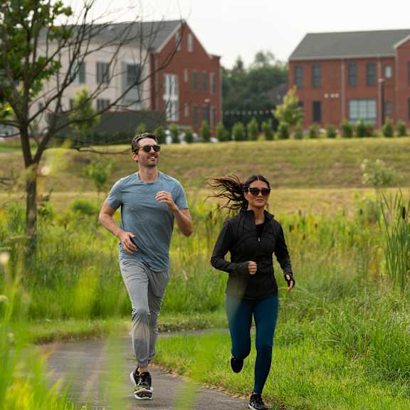 two people running on a path in a grassy field.