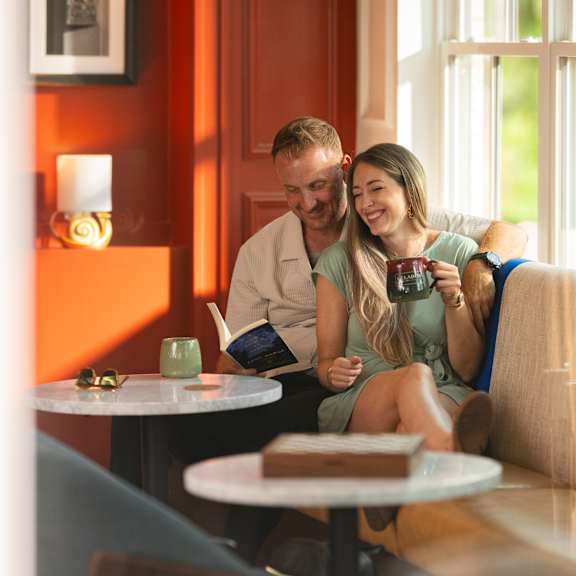 a man and woman are sitting on a couch, with the woman holding a camera.