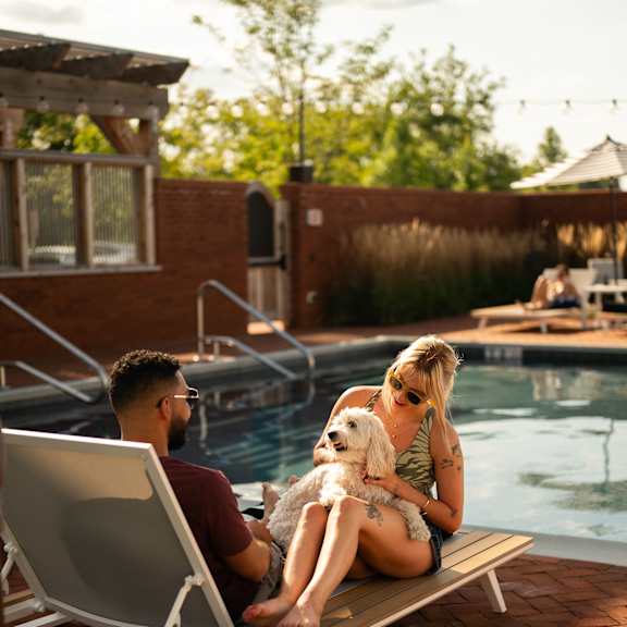 a man and a woman are sitting by a pool with a dog.