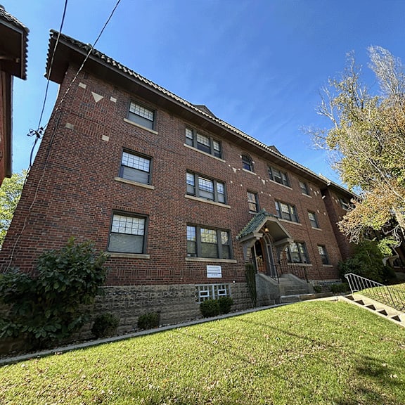 a red brick apartment building with a green lawn and a blue sky