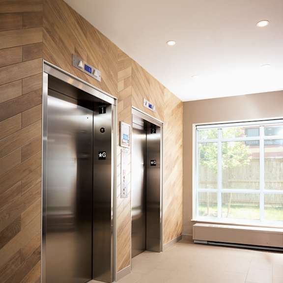 two stainless steel elevators in a hallway with wood paneling on the walls.