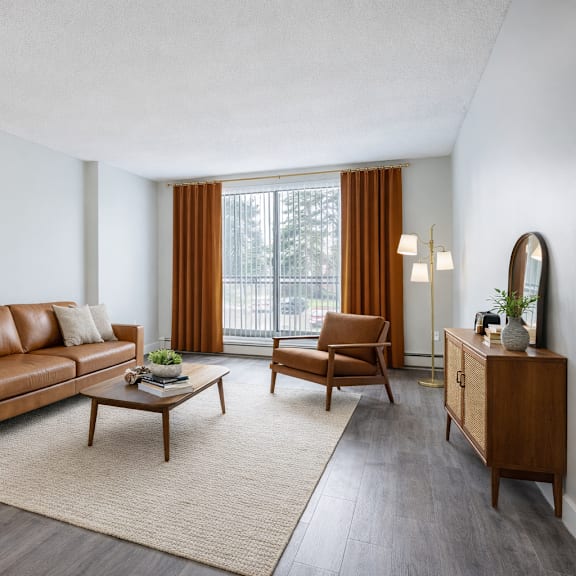 a living room with a brown leather sofa, a wooden coffee table, and a large window with orange curtains.