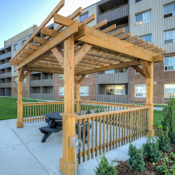 a wooden pergola is in front of a building with a bench underneath it  at platts crossing, london, on, n6h 4p4