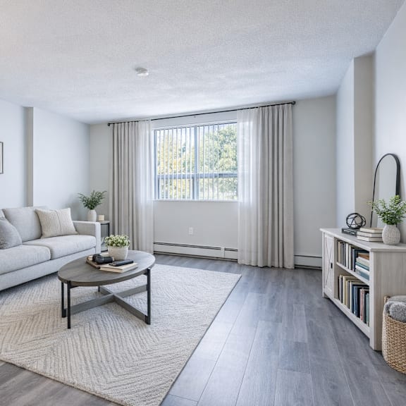a modern living room with a grey couch, a coffee table, and a large window with curtains.