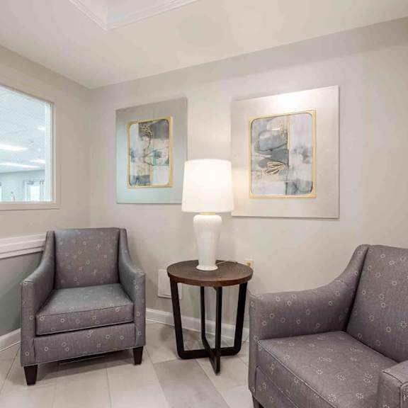 a grey chair sits in a waiting room with a table and another chair.