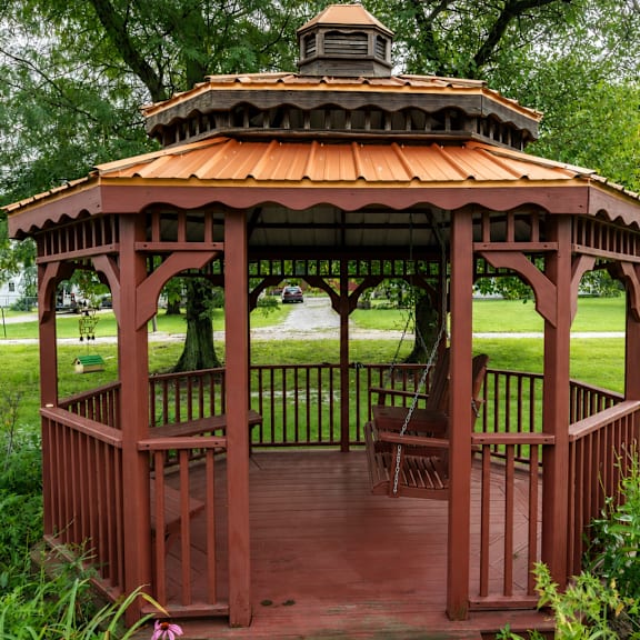 a gazebo with a red roof and wooden railing is surrounded by greenery.