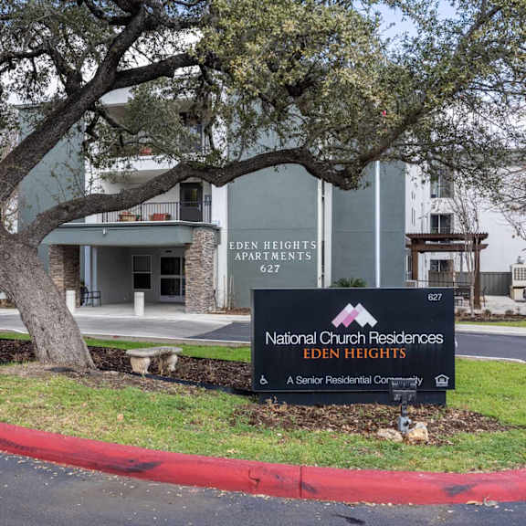 a sign for national church residences eden heights is in front of a tree.