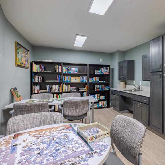 a room with a puzzle on the table and a bookshelf filled with books.