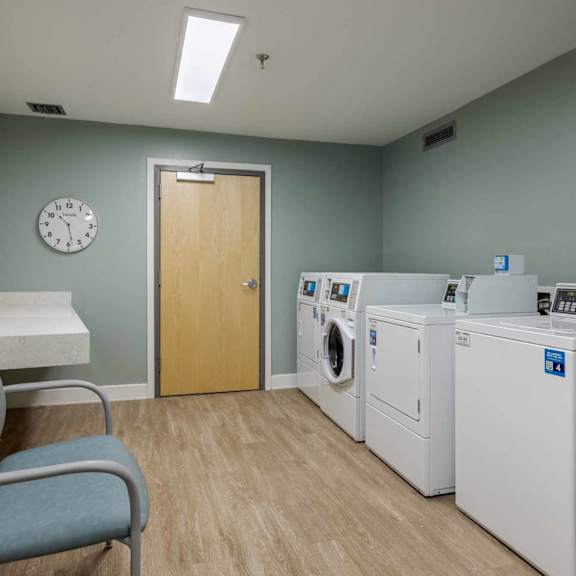 a laundry room with a chair, washing machine, dryer, and ironing board.