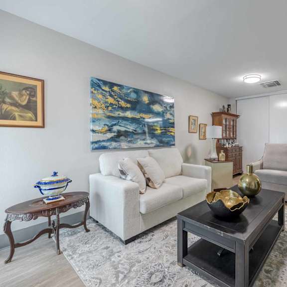 a living room with a white couch, a coffee table, and a painting on the wall.
