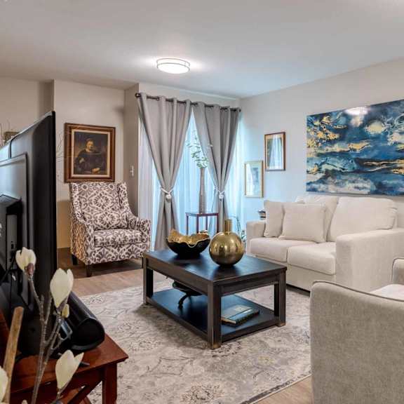 a living room with a white couch, a chair, a coffee table, and a painting on the wall.