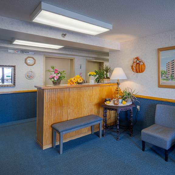 a waiting room with a bench, two chairs, a table with a lamp, and pictures on the wall.