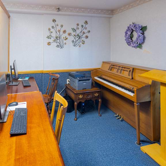 a room with a desk, computer, keyboard, and a piano.