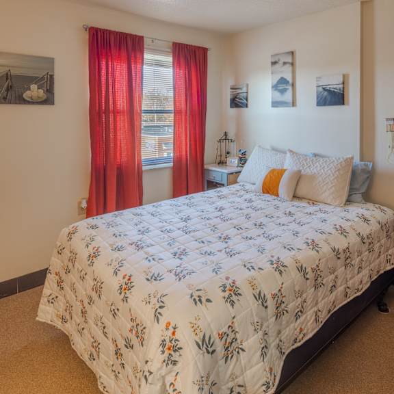 a bed with a floral patterned comforter is in a room with a red curtain.