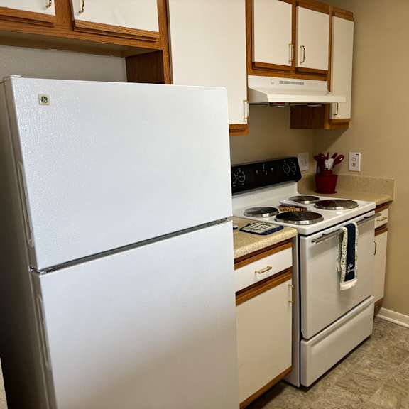 a white refrigerator stands in a kitchen with a stove and oven.