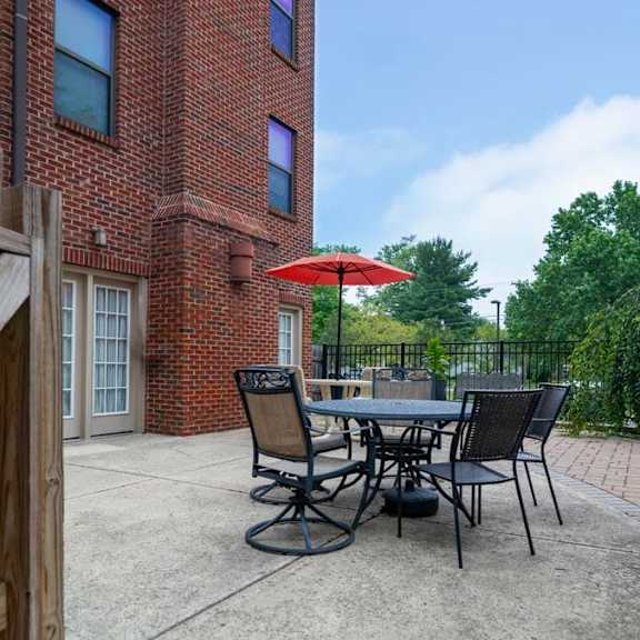 a patio with a table and chairs is surrounded by a brick building and trees.