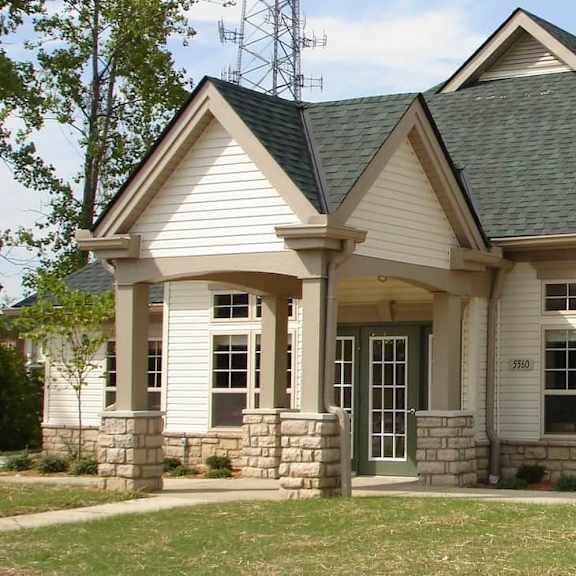 a white house with a green roof and a brick pillar in front.
