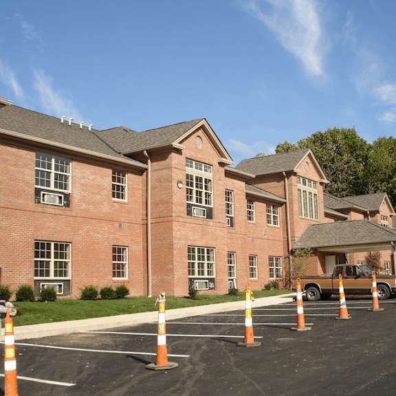 a parking lot in front of a red brick building with orange traffic cones around it.