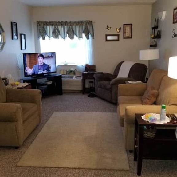 a living room with a television on, a couch, a chair, and a table.