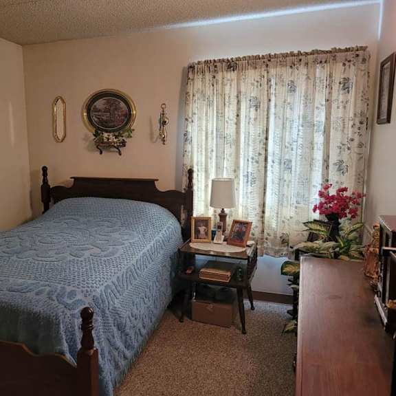 a bedroom with a bed, a table with a lamp, and a window with curtains.