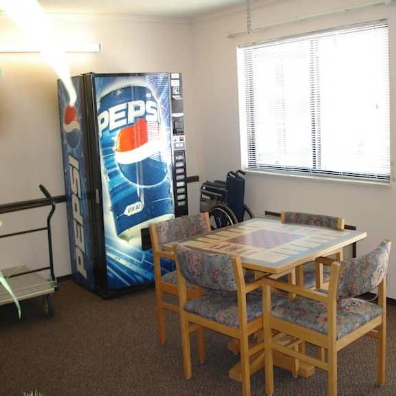 a pepsi vending machine sits next to a dining table in a room.