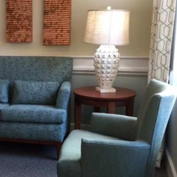 a grey couch sits next to a table with a white lamp on it.