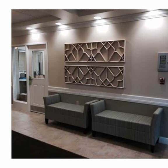 a wall with a decorative panel and two grey couches in front of it.