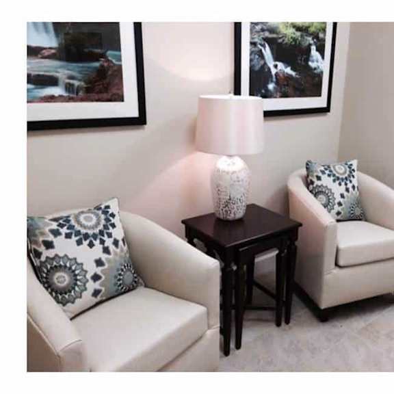 a living room with a white couch, a small table with a lamp, and two pictures on the wall.