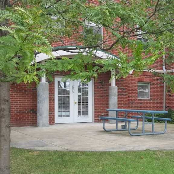 a red brick building with a white door and a bench under a tree.